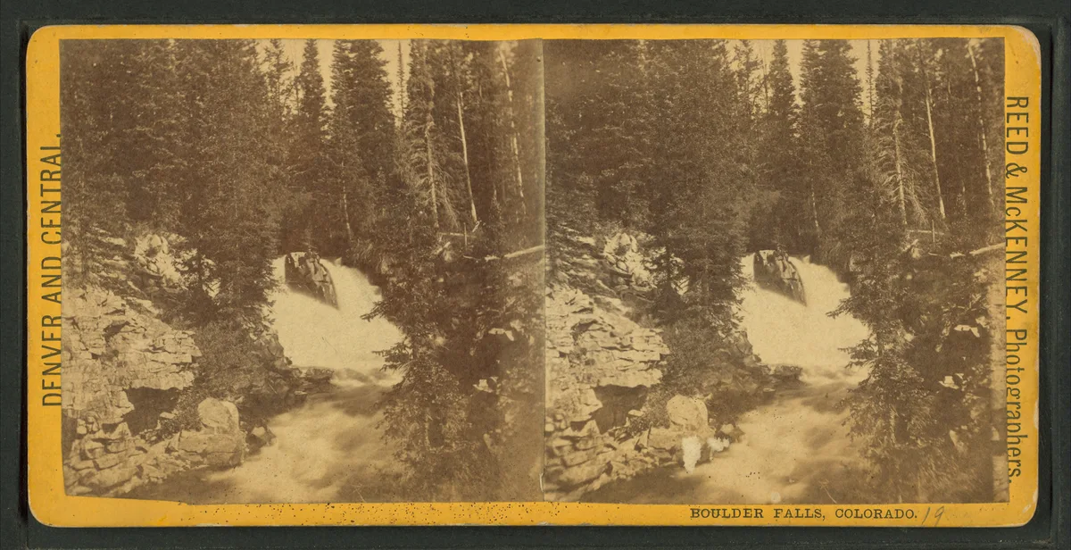 A sepia stereograph shows Boulder Falls spilling in a silky long exposure over a granite ledge into a narrow canyon, framed by dense evergreen forest and rough rock walls. The waterfall sits centered in the composition, with the creek flowing toward the foreground under soft morning light.