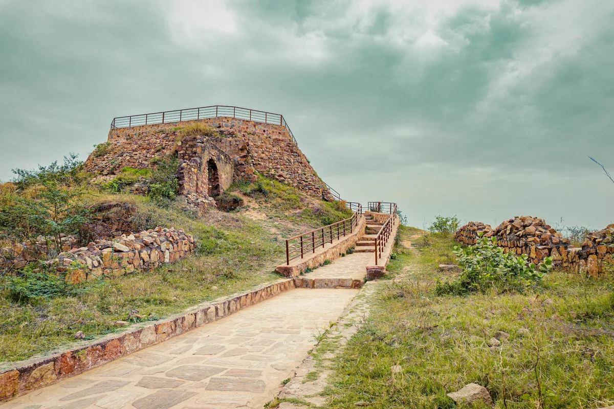 A stone lookout platform sits atop Horsetooth Rock, reached by a paved path and short stairway bordered by rustic stone walls and metal railings. Grassy foothills and a cloudy sky frame the rugged outcrop in soft, muted light.